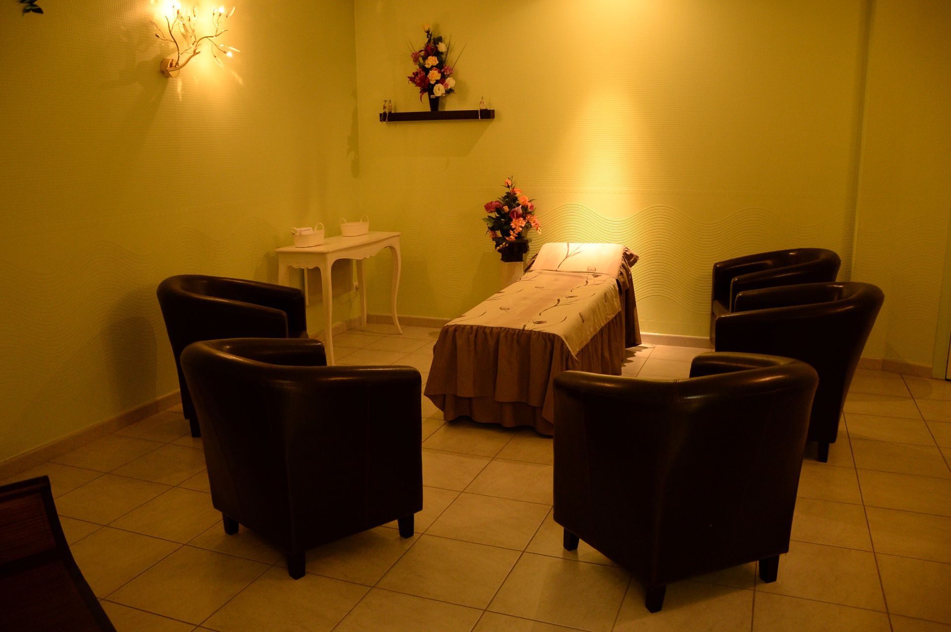 Une salle de cérémonie : six fauteuils marron entourent un lit, des fleurs sur une table et une étagère.