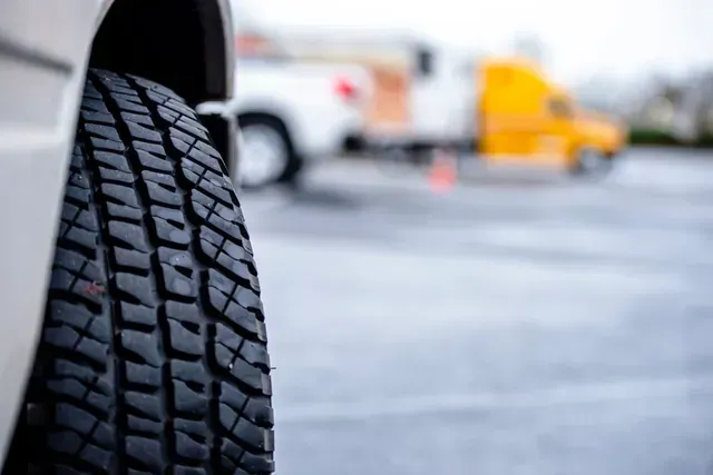 Primer plano de la banda de rodadura de un neumático sobre una carretera mojada, con vehículos borrosos al fondo.