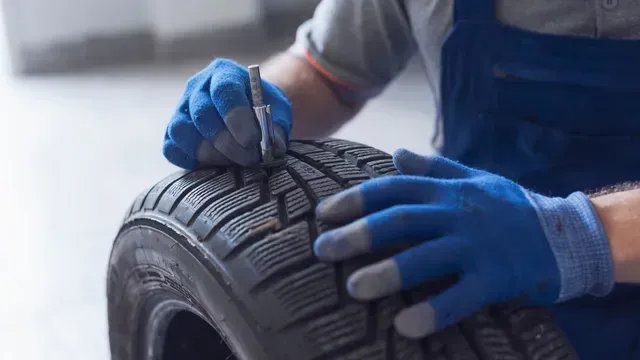 Manos enguantadas inspeccionando la banda de rodadura de un neumático de coche en un taller.