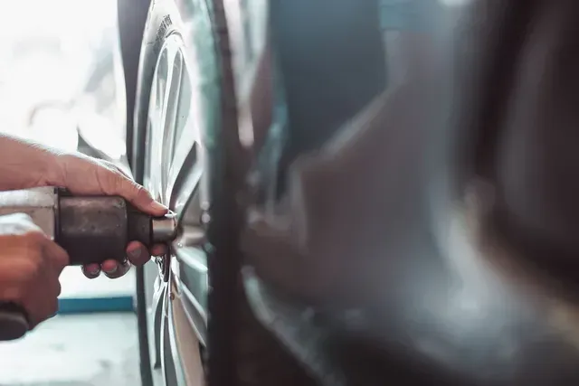 Manos usando una llave inglesa para apretar la tuerca de una rueda de coche en un garaje.