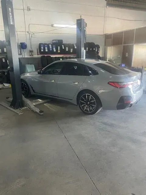 Sedán plateado sobre un elevador de coches dentro de un taller de reparación de automóviles.