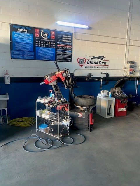 Taller de reparación de automóviles con máquina para cambiar neumáticos, herramientas, mangueras y letreros en las paredes.