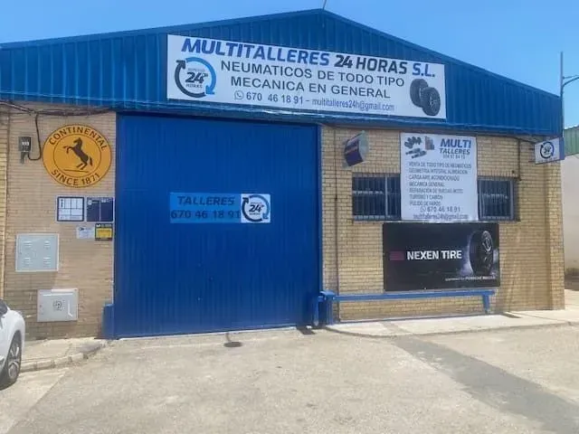 Taller mecánico con fachada metálica azul, letreros y puerta cerrada en una calle soleada.