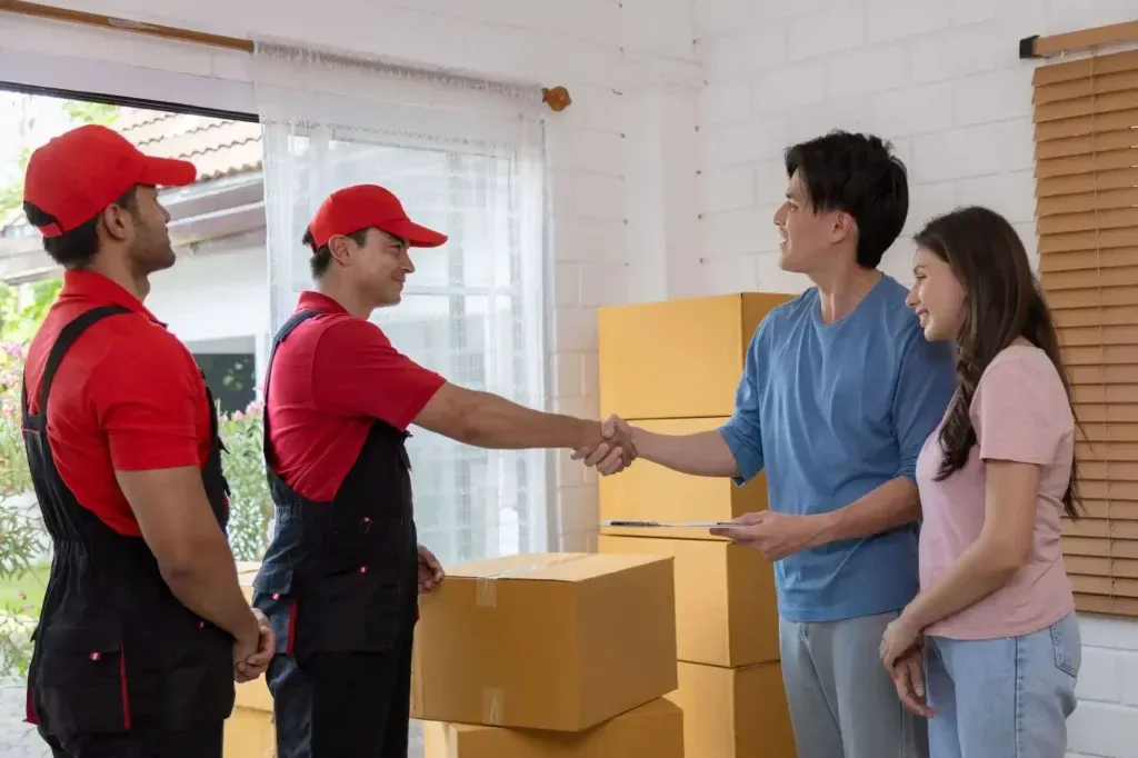 Los transportistas estrechan la mano a una pareja junto a cajas de cartón apiladas en una casa.
