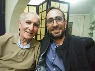 Dos hombres posan para una fotografía juntos en una sala de estar.