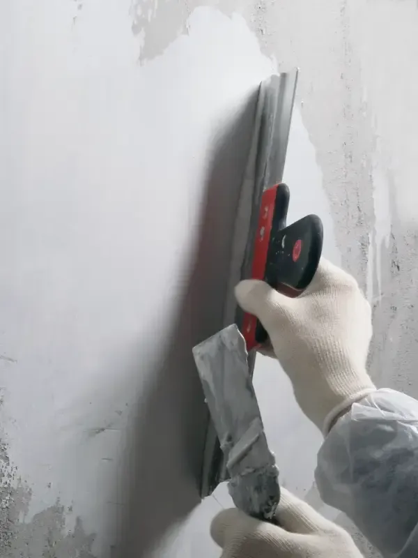 Una persona con guantes de trabajo utiliza una herramienta alisadora para aplicar masilla para juntas a una pared.