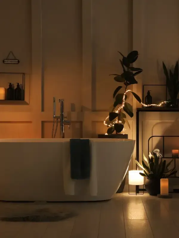 Un baño acogedor con iluminación tenue, que cuenta con una bañera blanca independiente, plantas en macetas