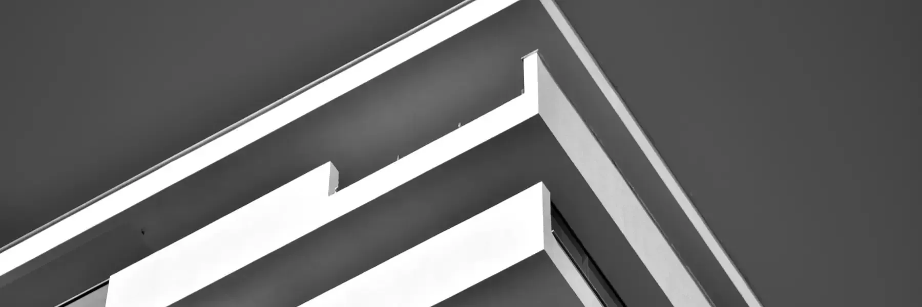 Detalle arquitectónico abstracto de estructuras blancas angulares y superpuestas sobre un fondo oscuro y minimalista.