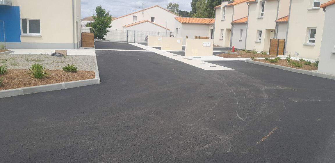 Route asphaltée neuve devant des bâtiments beiges aux toits orange.