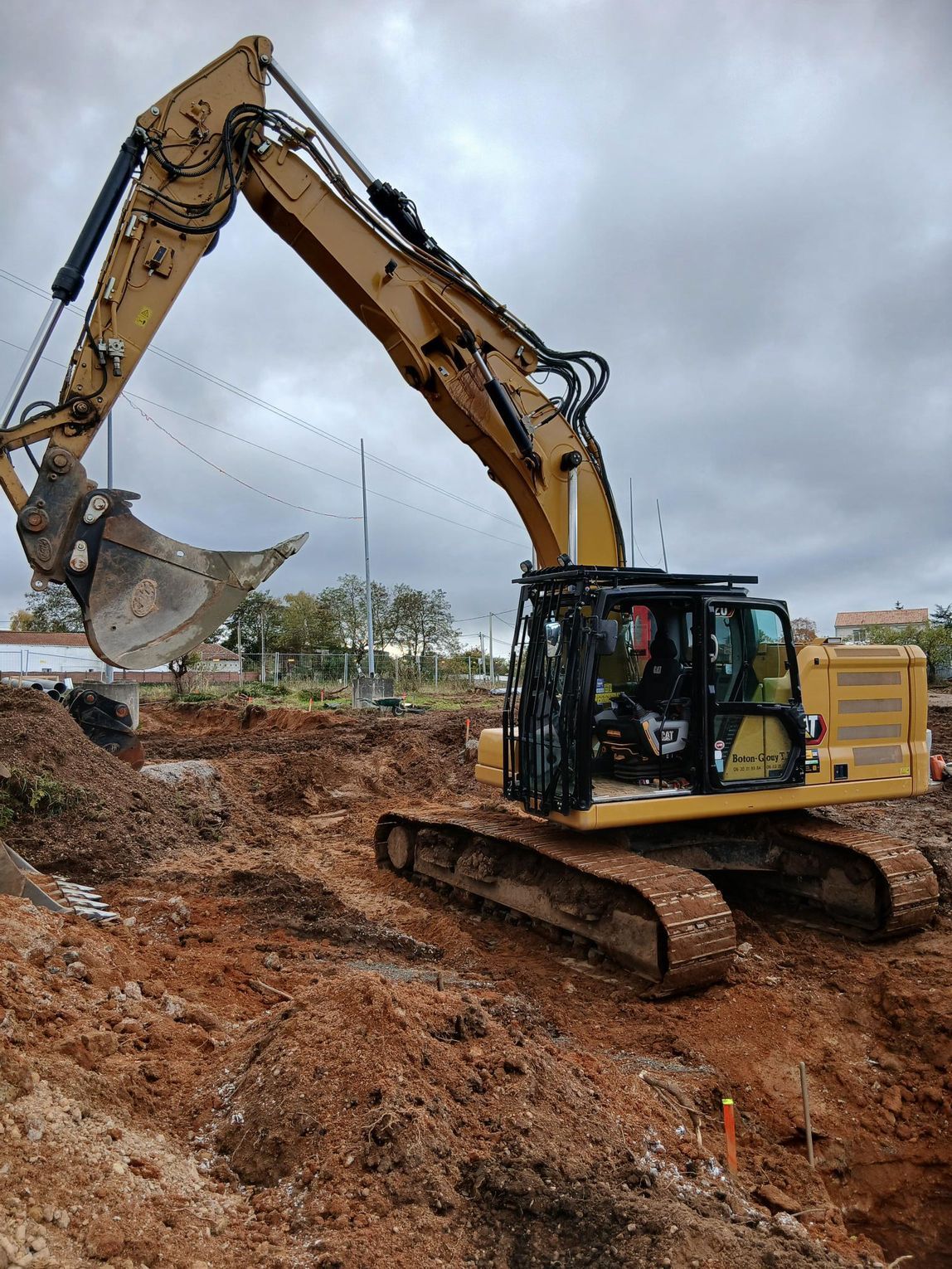 Une pelleteuse jaune creuse dans un chantier boueux sous un ciel nuageux.