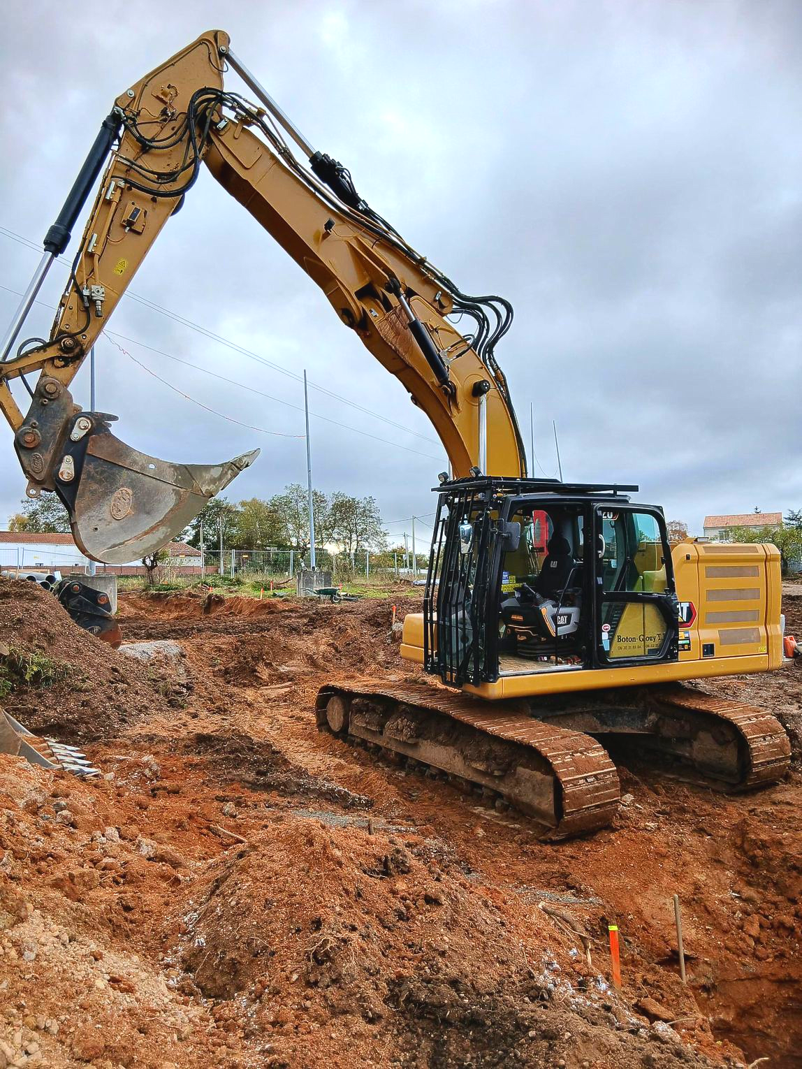 Une pelleteuse jaune creuse dans un terrain vague sous un ciel couvert.