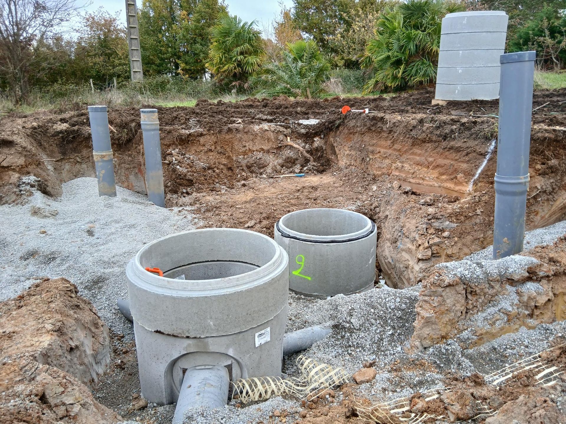 Chantier de construction avec fosses septiques et canalisations en béton dans une zone excavée.