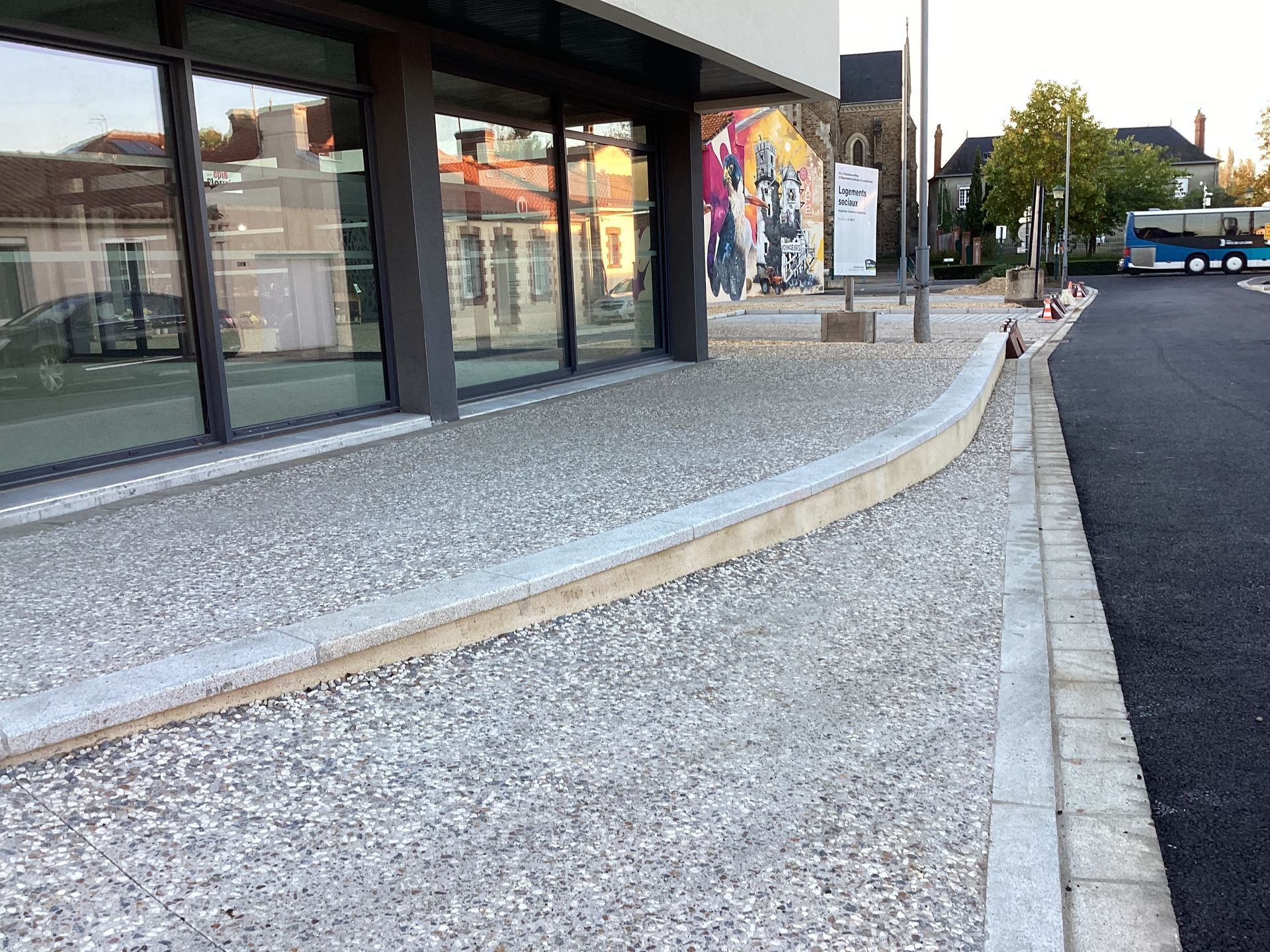 Un bâtiment moderne avec un trottoir incurvé devant et un bus en arrière-plan.