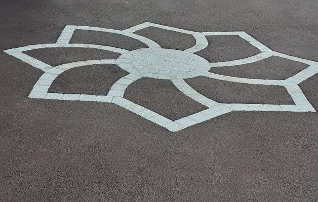 Motif floral en pierre blanche, incrusté dans de l'asphalte foncé.