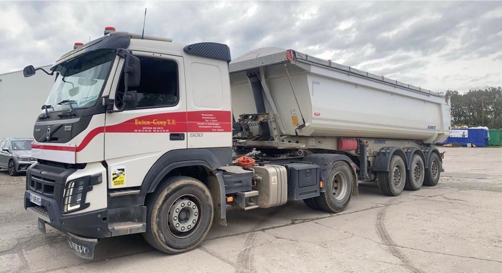 Camion-benne blanc à rayures rouges stationné sur un terrain gravillonné.