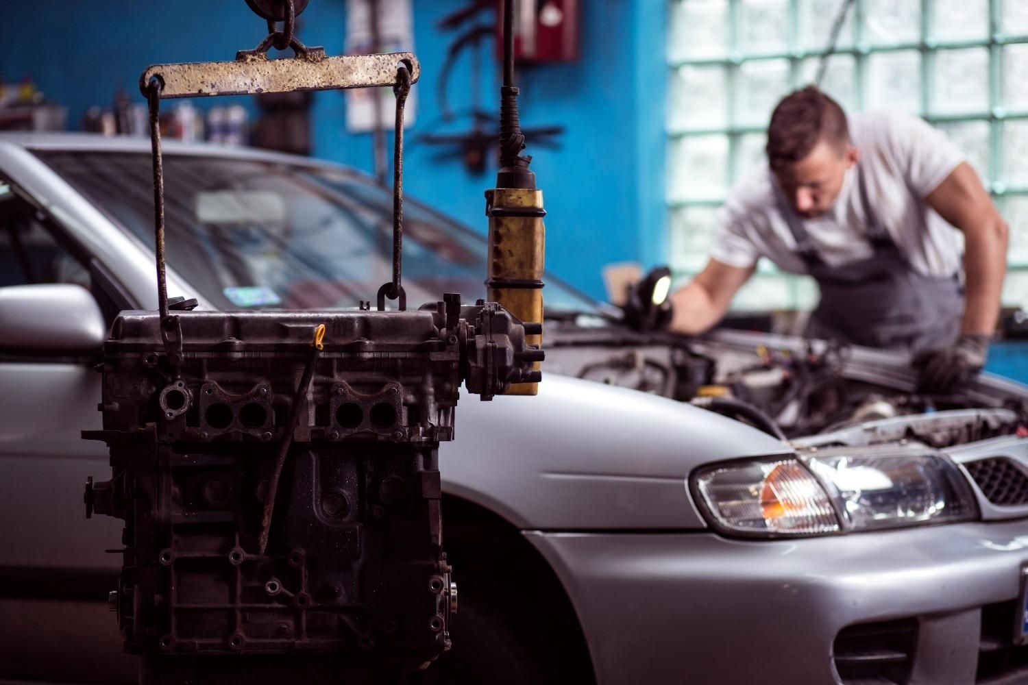Un mecánico trabaja en un taller mecánico, en el motor de un coche que está suspendido por una grúa frente al capó abierto.