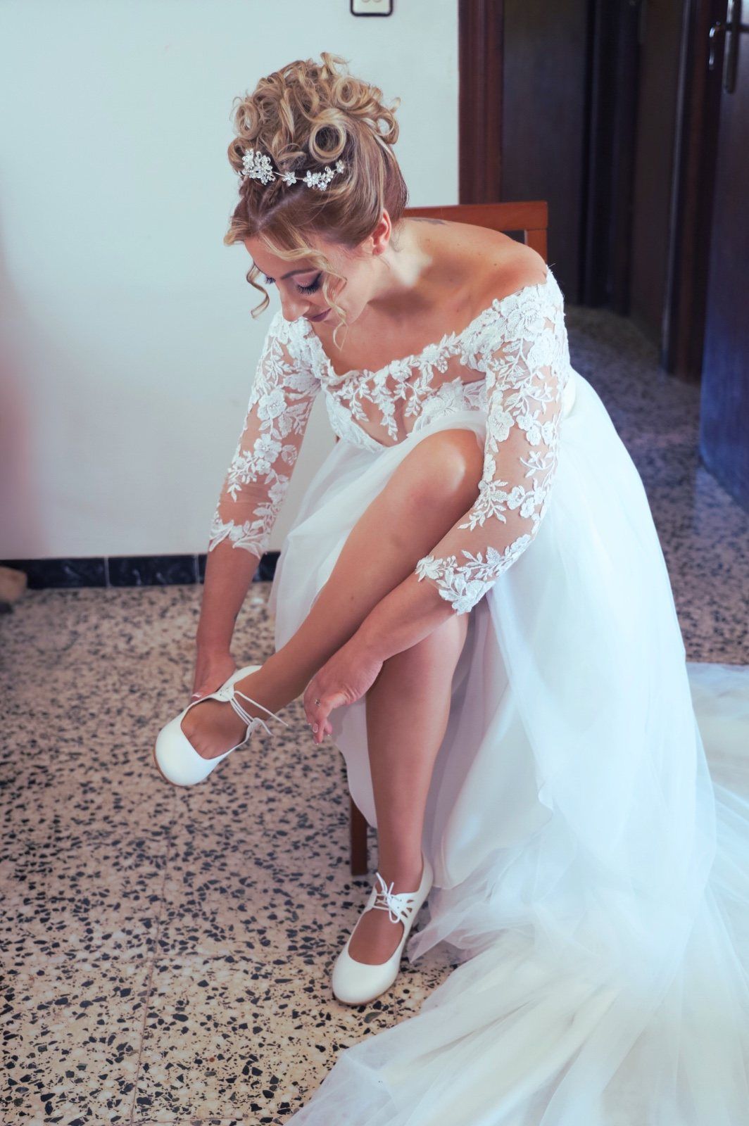 Novia con vestido de novia blanco poniéndose zapatos blancos, preparándose para la ceremonia.