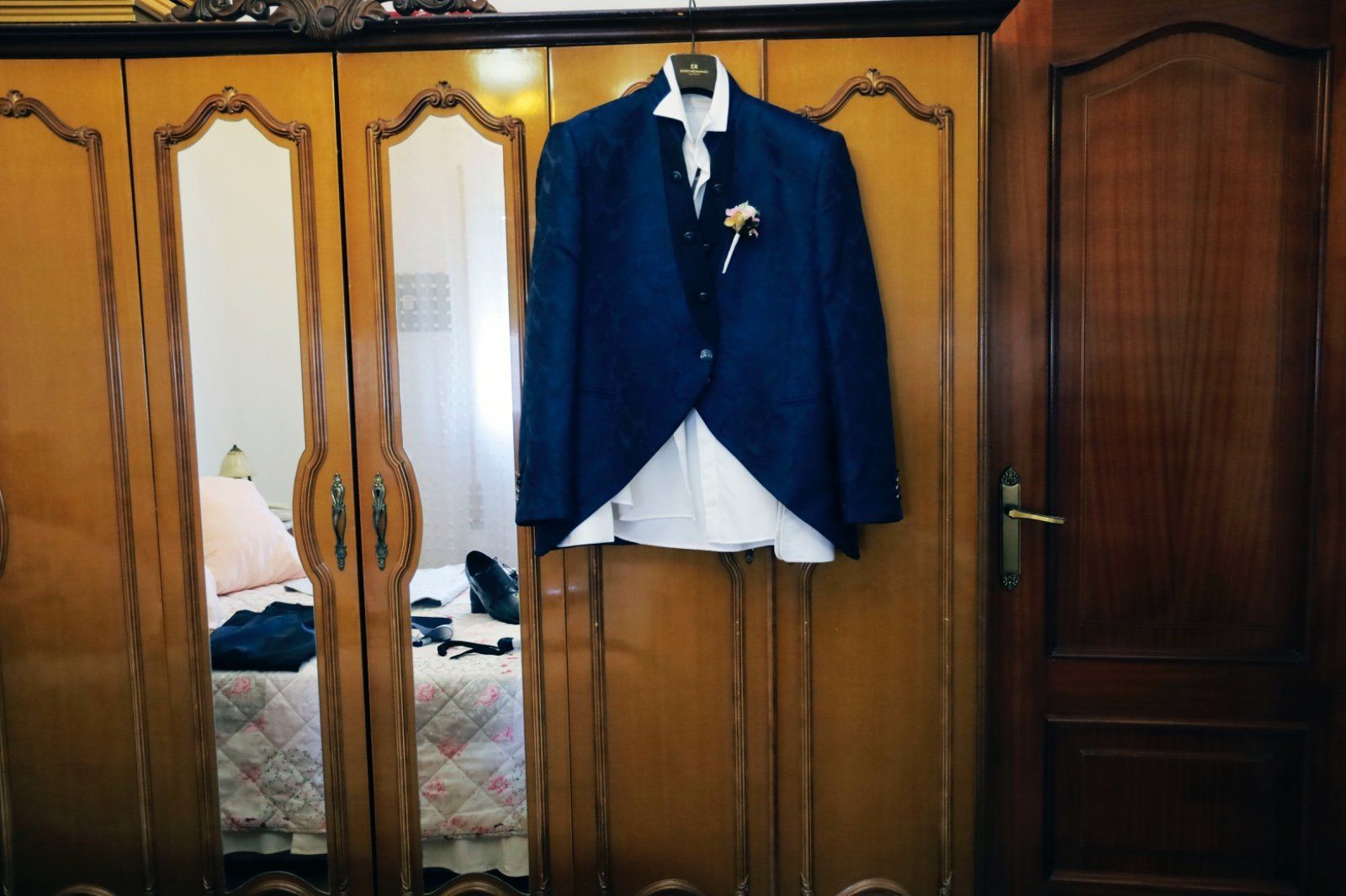 Una chaqueta de traje azul y una camisa blanca colgadas en un armario de madera con espejos.