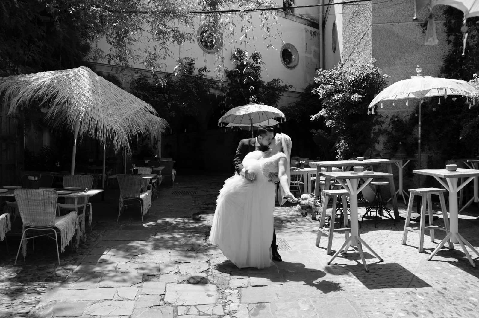 Fotografía en blanco y negro de una pareja de novios bailando al aire libre bajo sombrillas.