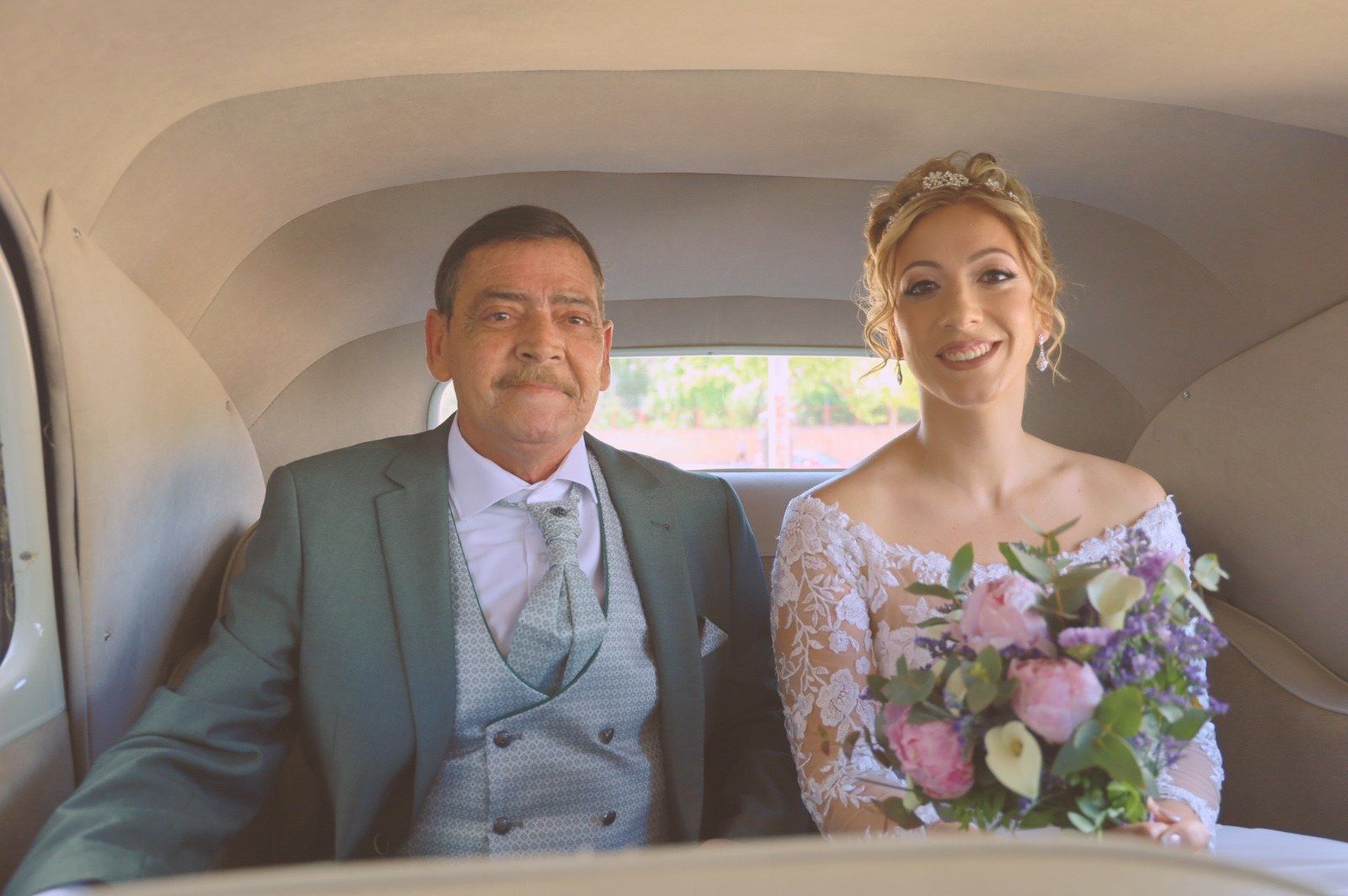 La novia y su padre están sentados en la parte trasera de un coche clásico. 