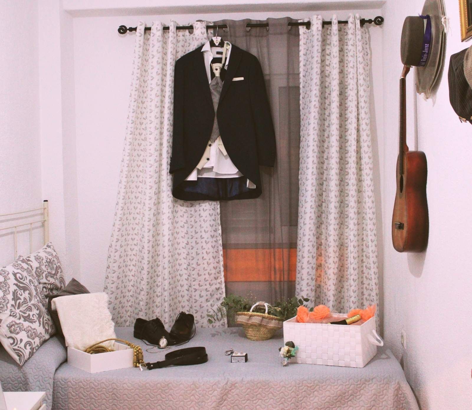 Un traje colgado frente a una ventana, con una cama enfrente. Los accesorios están dispuestos sobre la cama.