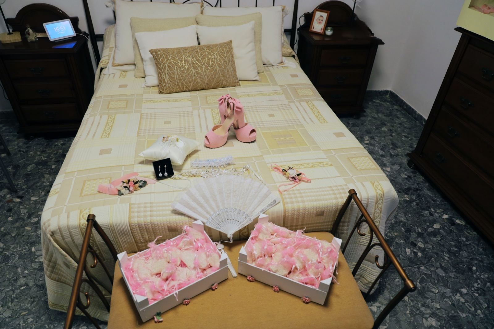 Cama con accesorios de boda: zapatos, abanico, joyero y cajas de flores, en ambiente de dormitorio.