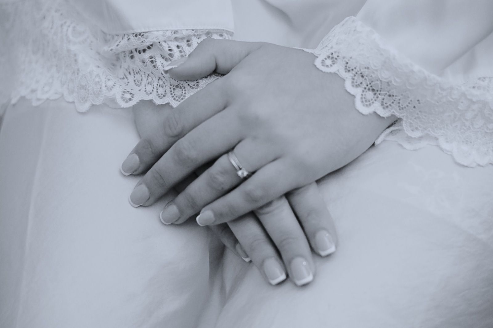 Manos de mujer, una de ellas con un anillo, apoyadas sobre una prenda blanca con ribete de encaje.