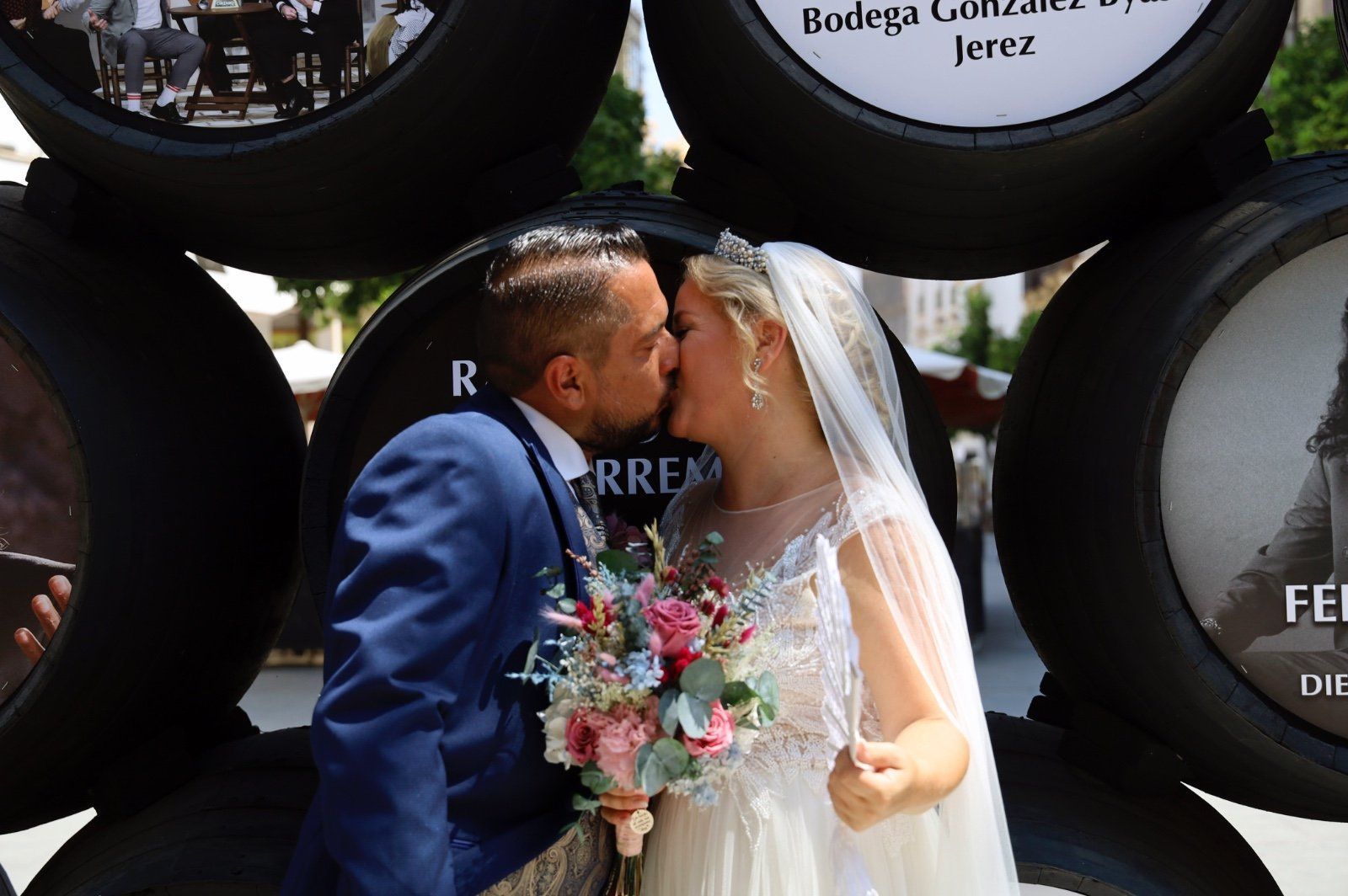 Una novia y un novio se besan frente a barriles de vino apilados.