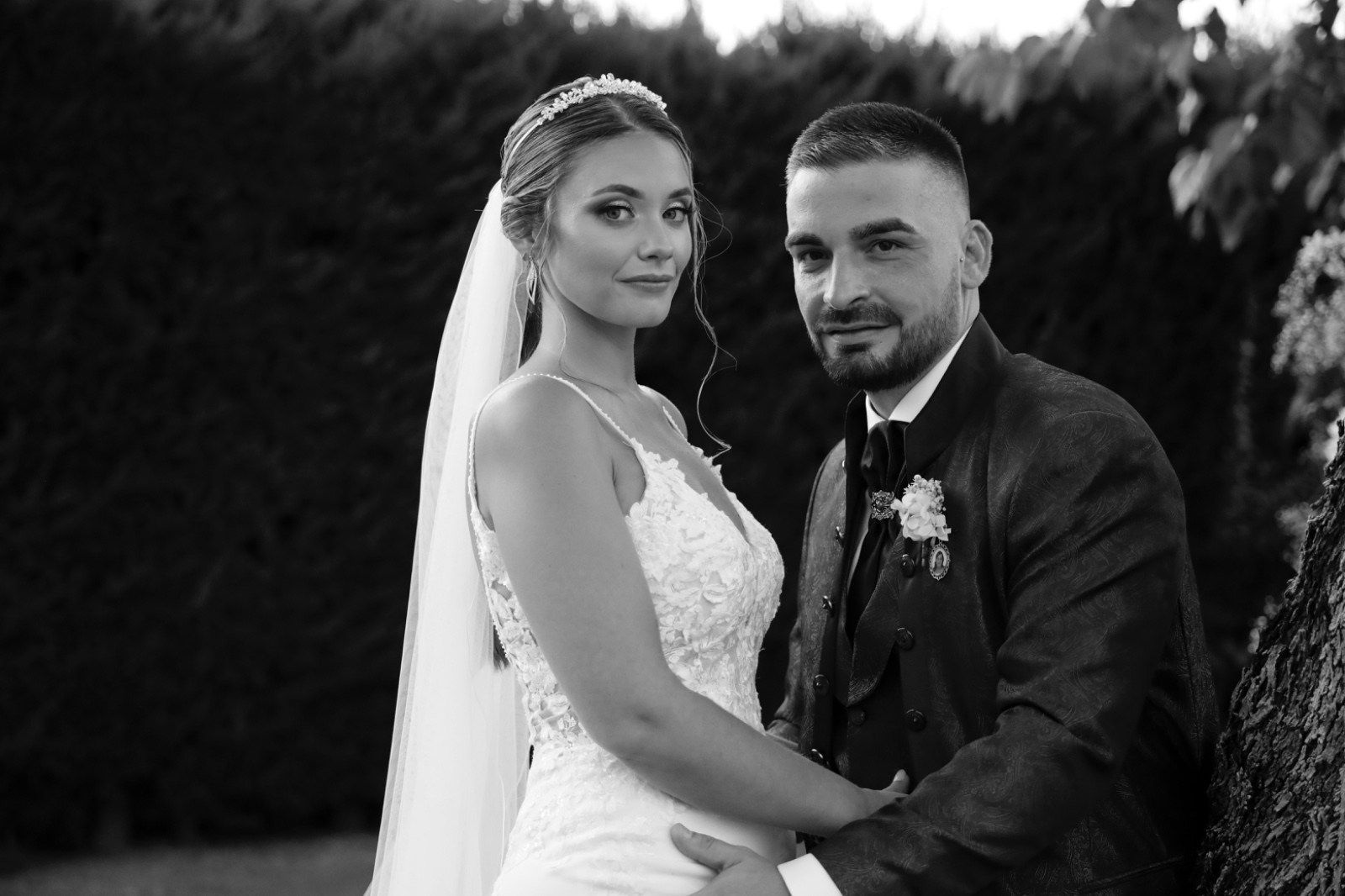 Novios posando para una foto de boda en blanco y negro. La mujer lleva vestido y velo, el hombre traje.