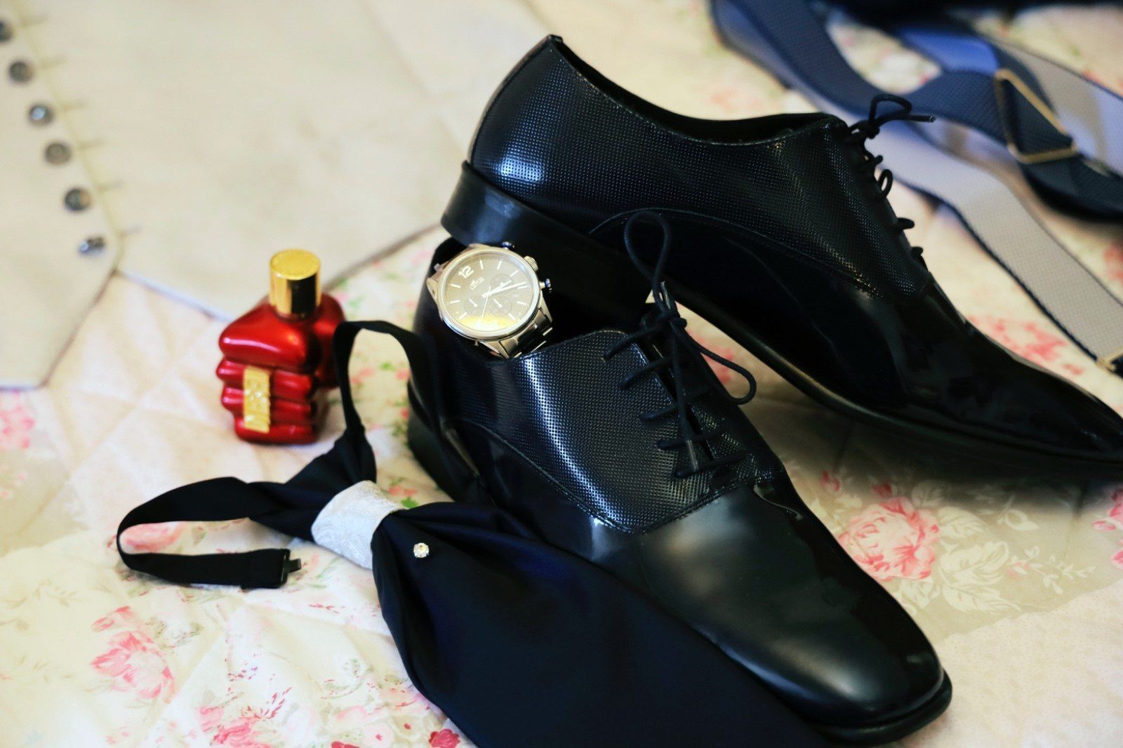 Ropa formal: zapatos de vestir negros, reloj, corbata, colonia y chaleco sobre fondo floral.