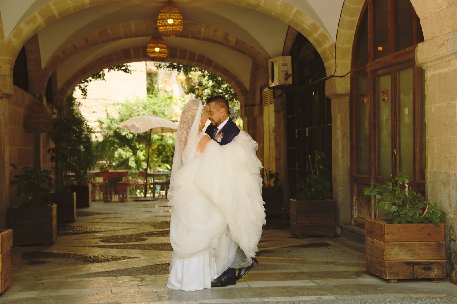 Los novios se abrazan bajo un arco. La novia lleva un vestido blanco amplio.