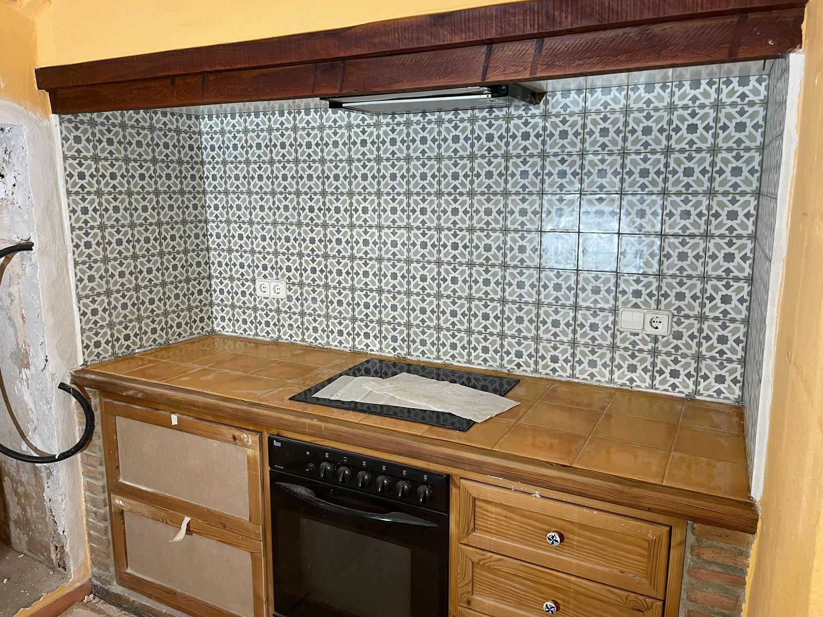 Cocina con gabinetes y encimera de madera, salpicadero de azulejos estampados y horno.