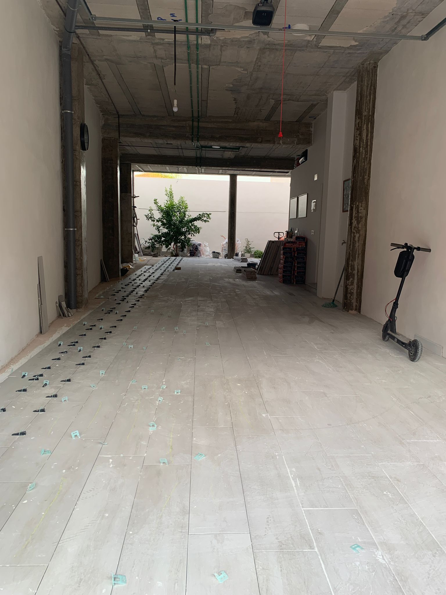 Vista interior de una obra con entrada abierta. Suelo y paredes grises, con una moto a la derecha.