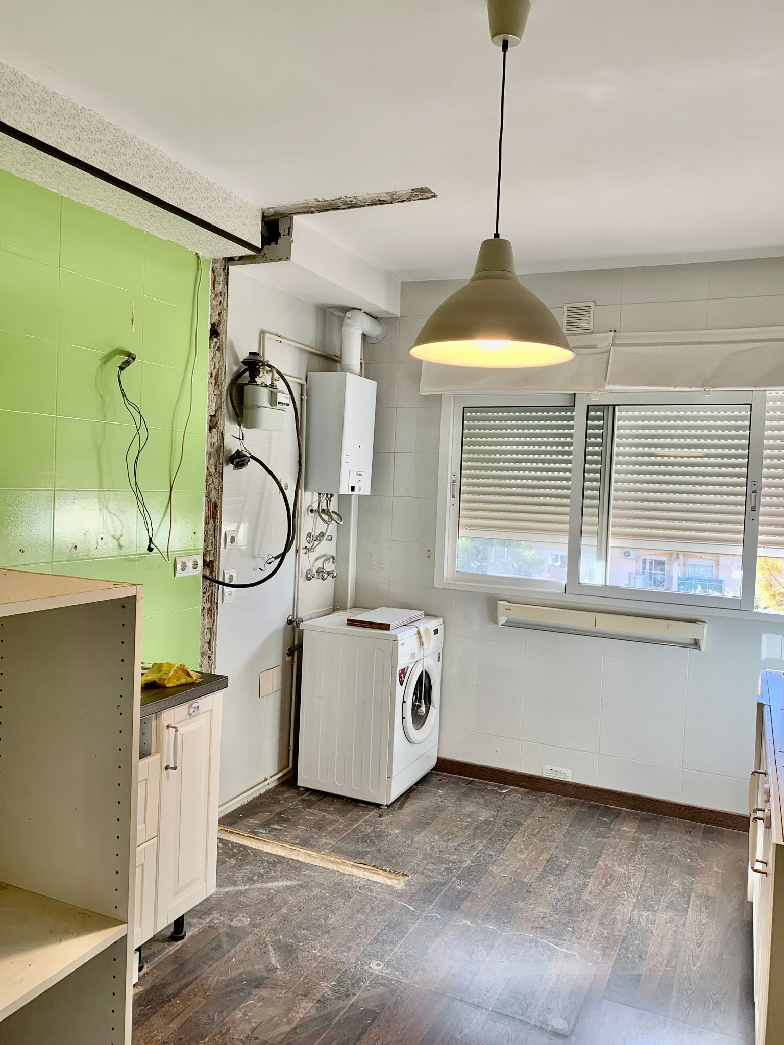 Cocina con lavadora, calentador de agua y lámpara colgante, en habitación con pared verde.