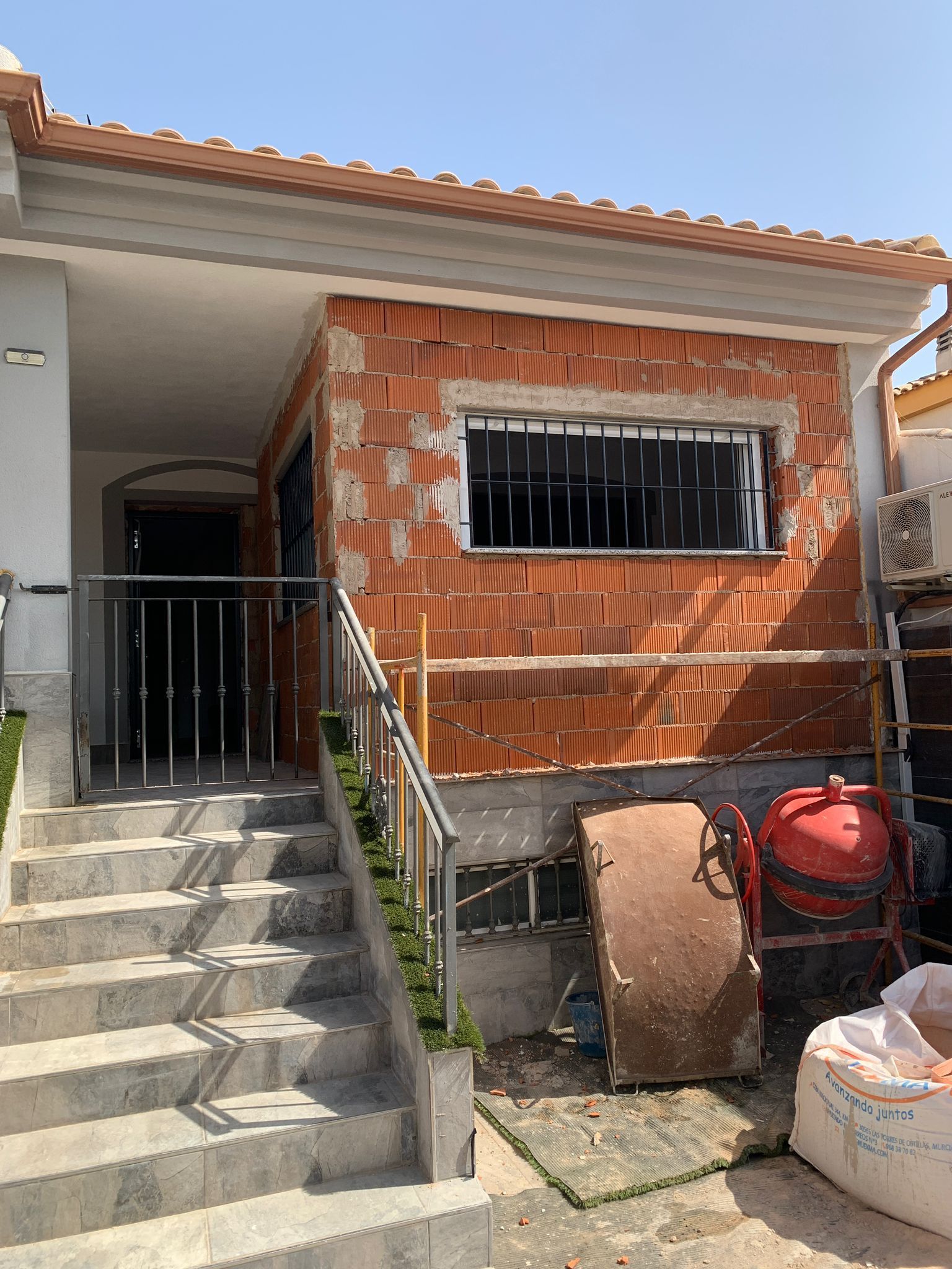 Edificio de ladrillo en construcción con escaleras, ventana enrejada y materiales de construcción.