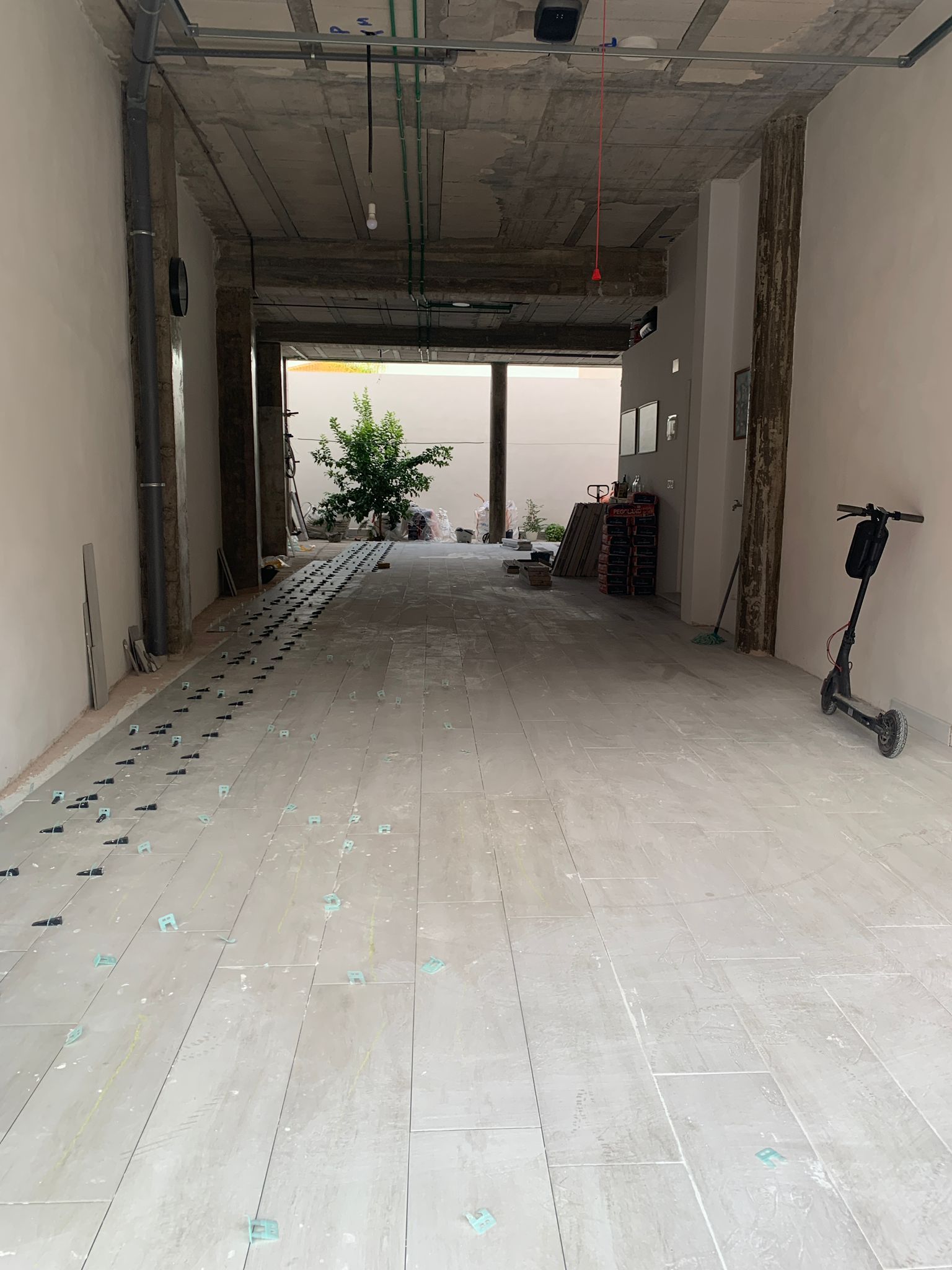 Un espacio interior vacío e inacabado, con abertura al exterior. Incluye scooter, vigas a la vista y materiales.