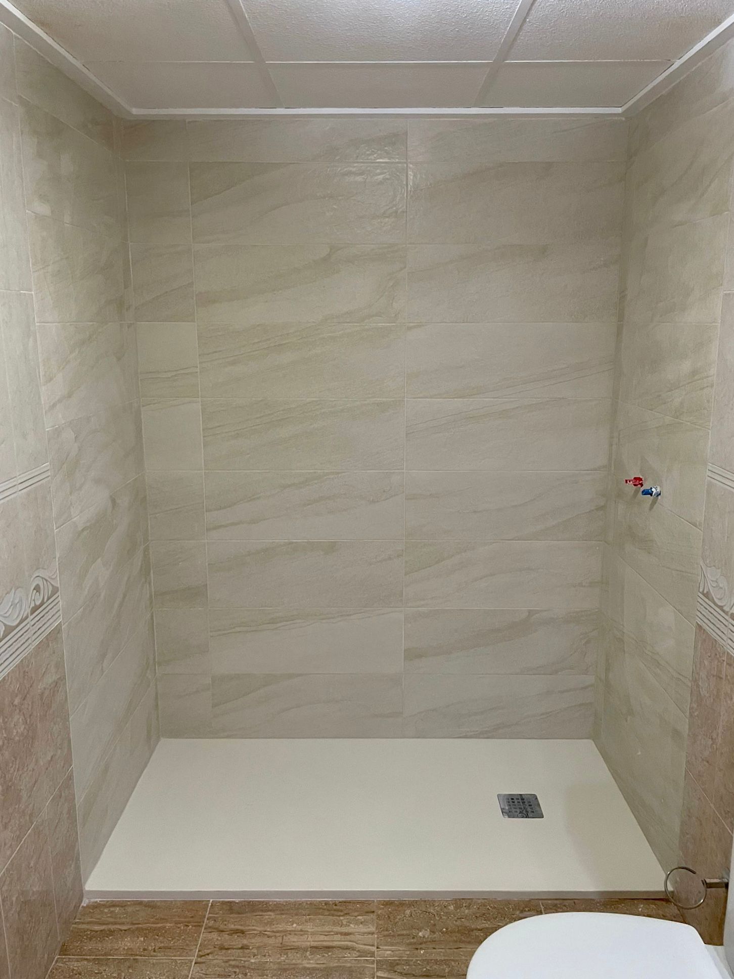 Cabina de ducha con azulejos de color beige y marrón y base de ducha de color blanco.