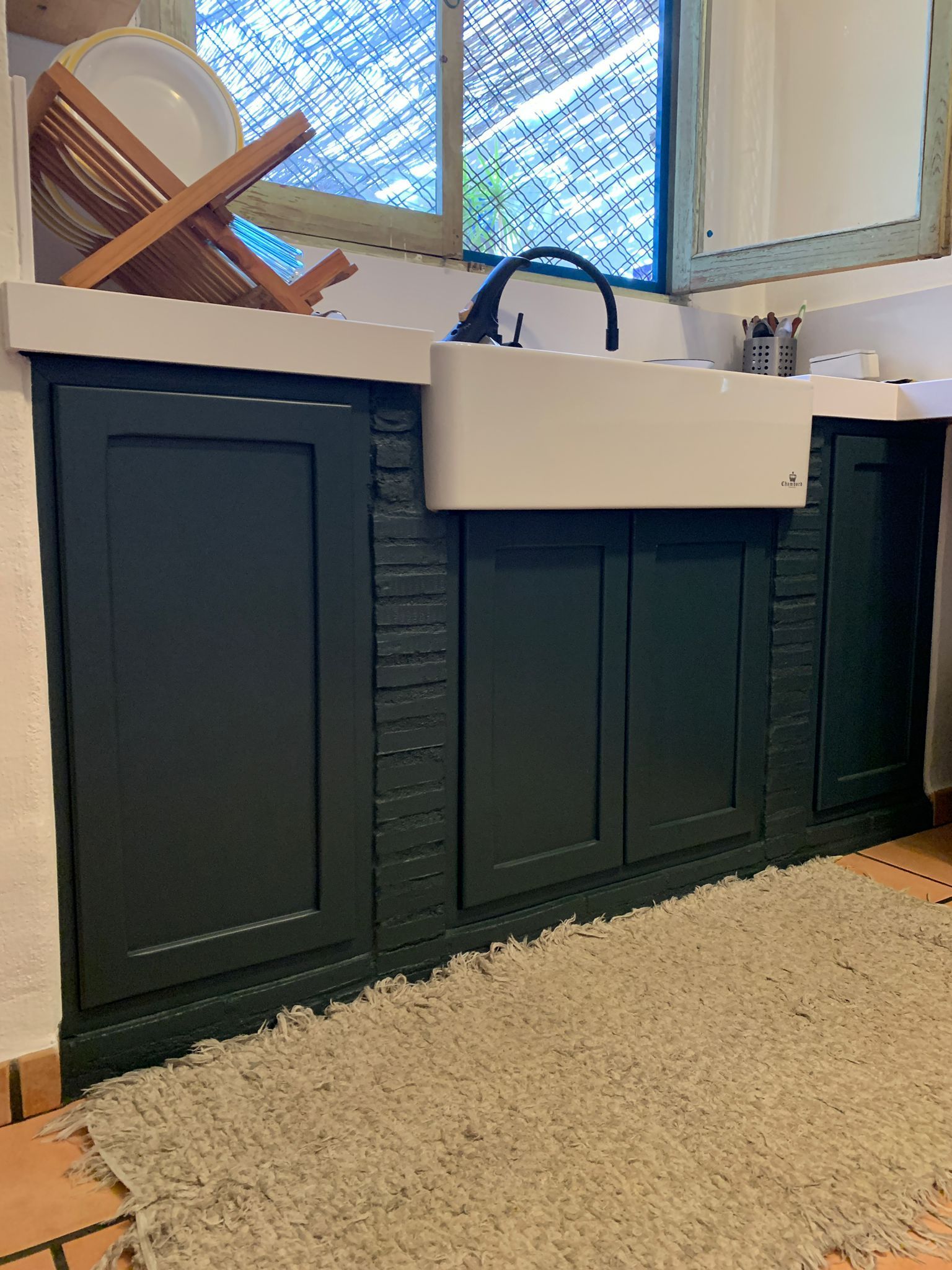 Gabinetes de cocina de color verde oscuro con fregadero y encimera de color blanco y alfombra clara en el frente.