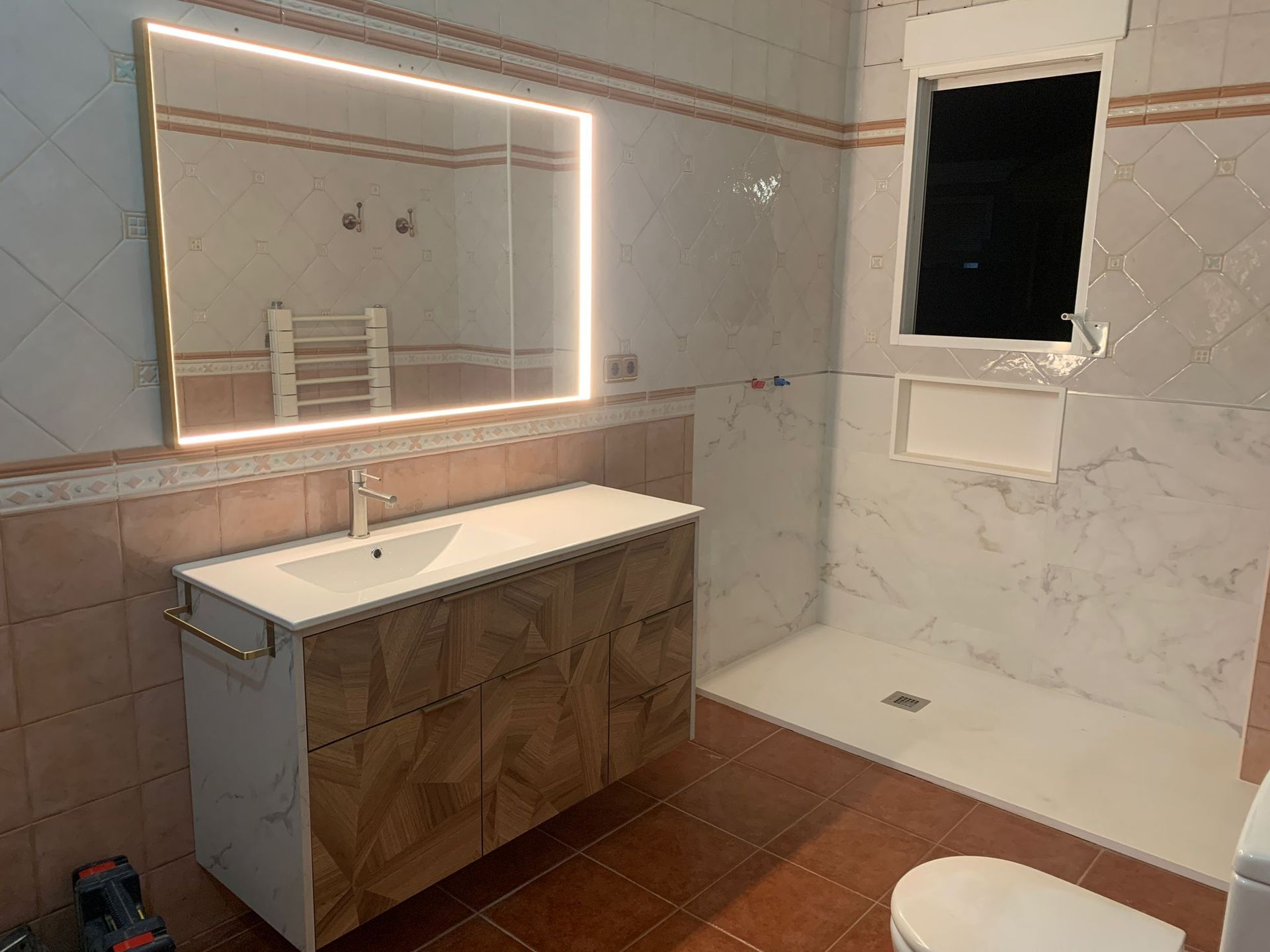 Baño con tocador, espejo iluminado, ducha e inodoro; paredes con azulejos.