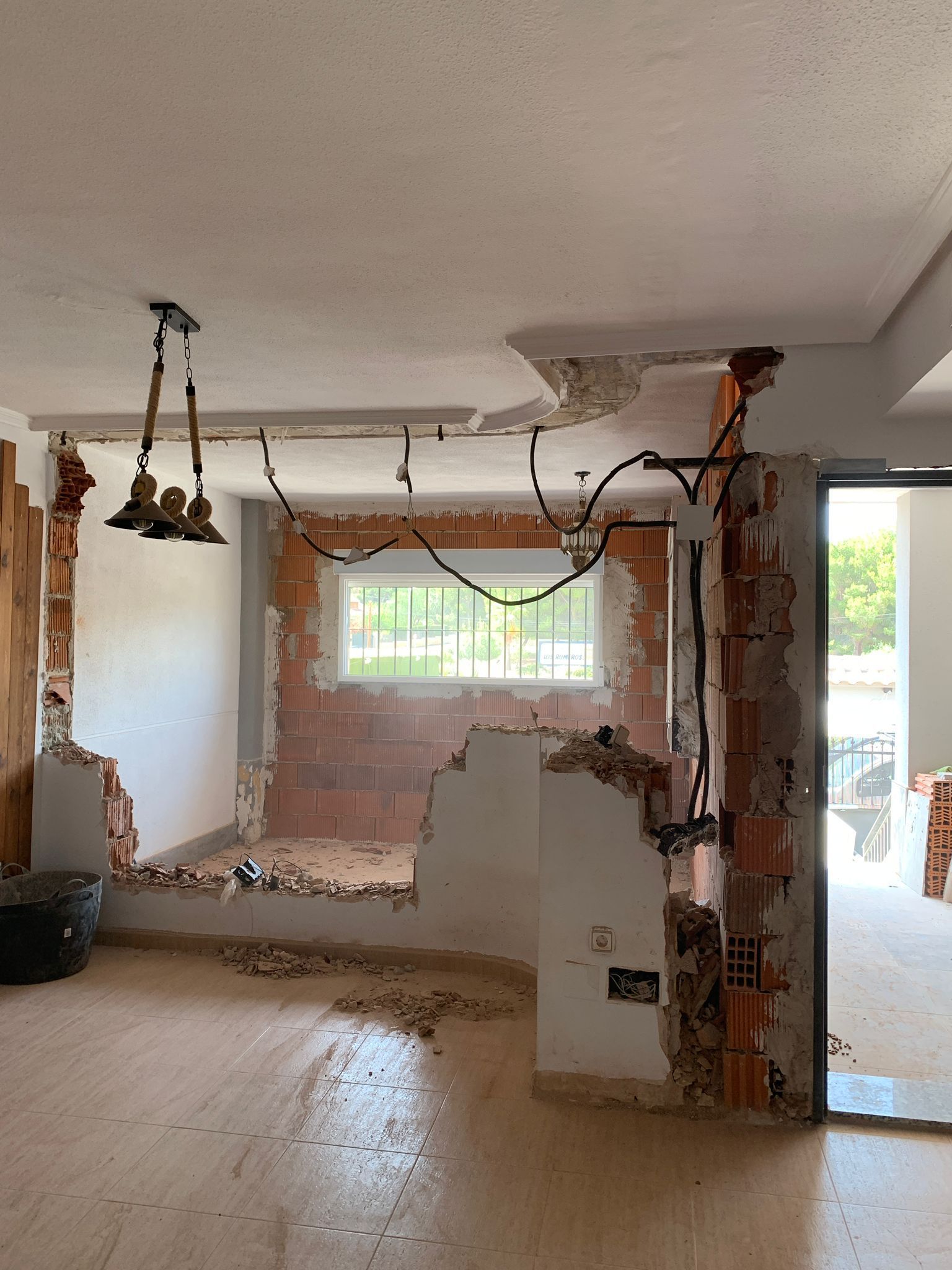 Demolición interior en progreso; ladrillos expuestos, cableado eléctrico, escombros y una ventana.