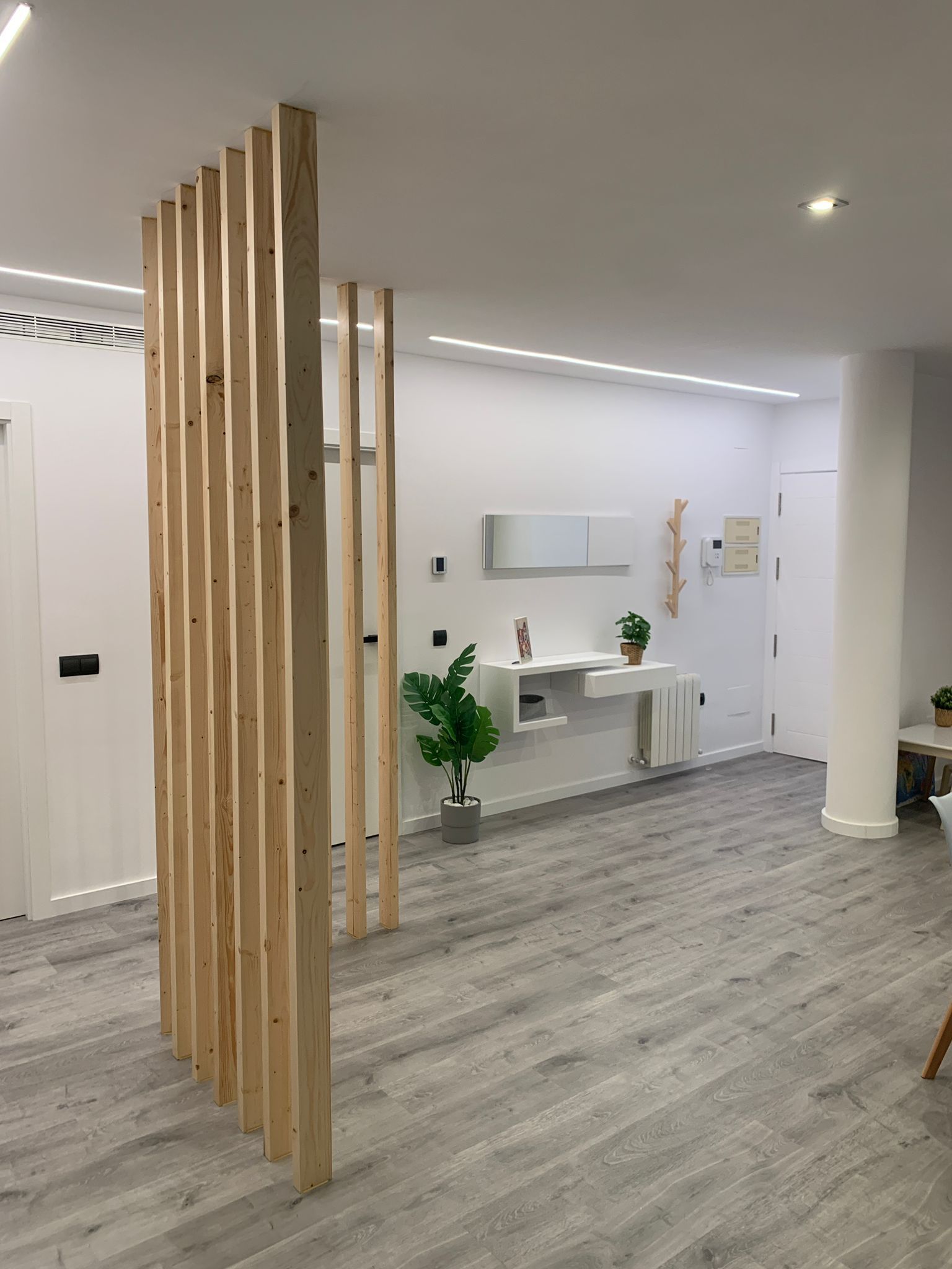 Biombo de listones de madera en un apartamento moderno. Suelo gris, paredes blancas y tocador empotrado.