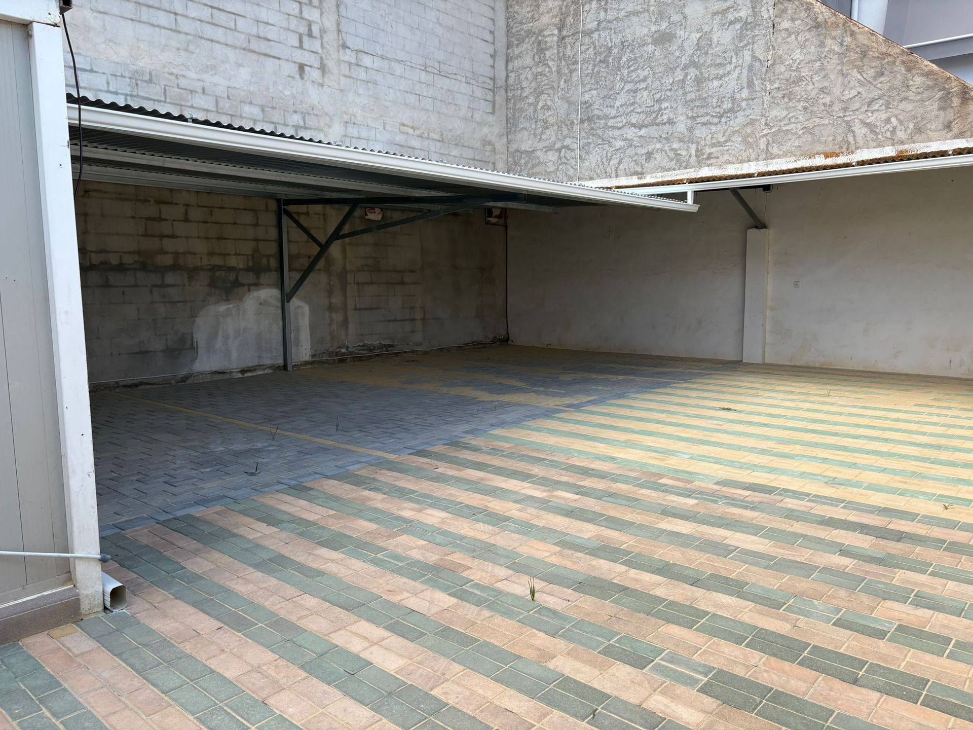 Espacio vacío, cubierto y al aire libre con suelo de ladrillo. Ladrillos grises y verdes cubren el suelo. Paredes y techo grises.