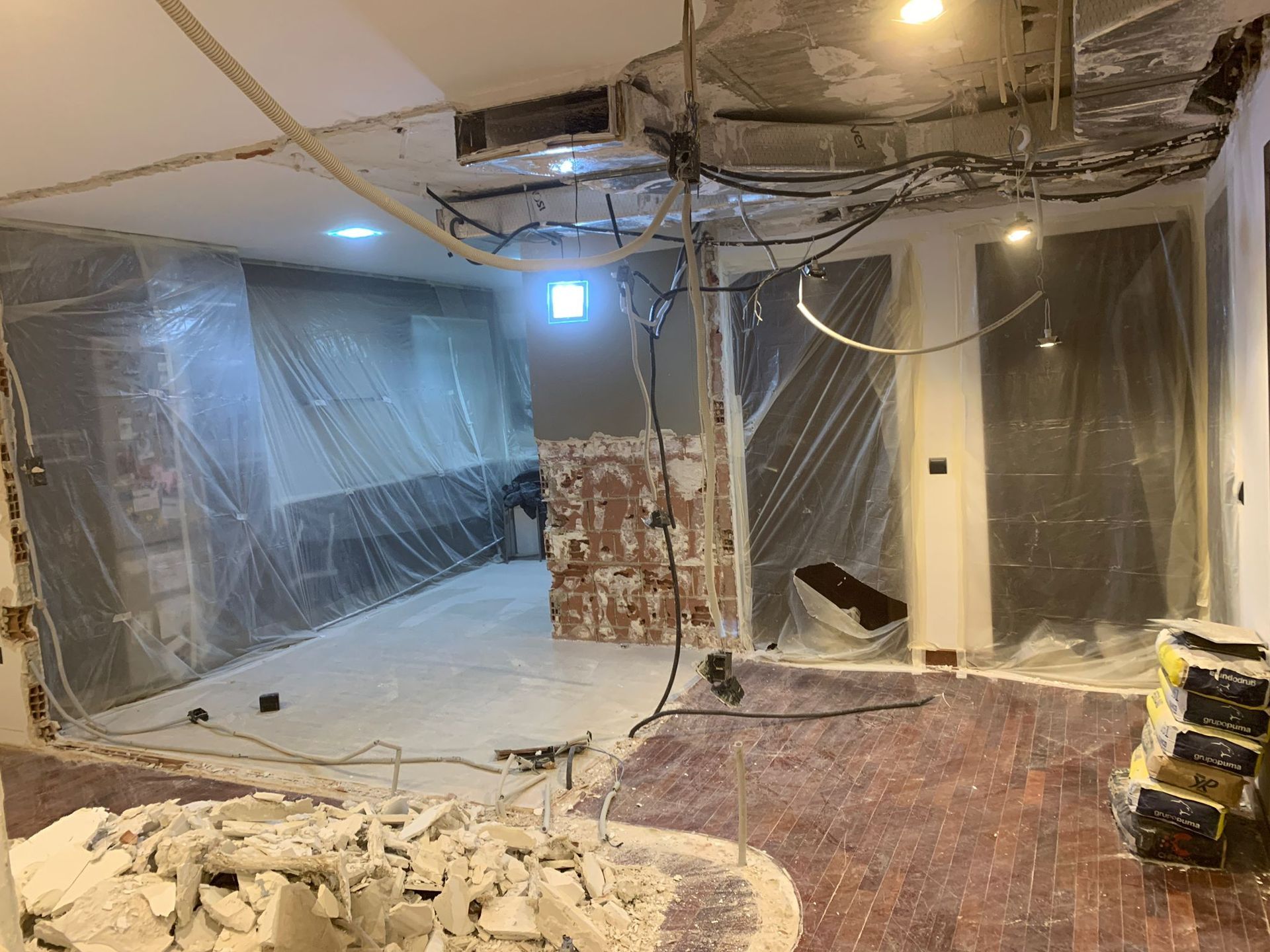 Habitación en remodelación, paredes cubiertas con plástico. Escombros en el suelo, cableado expuesto, obras.