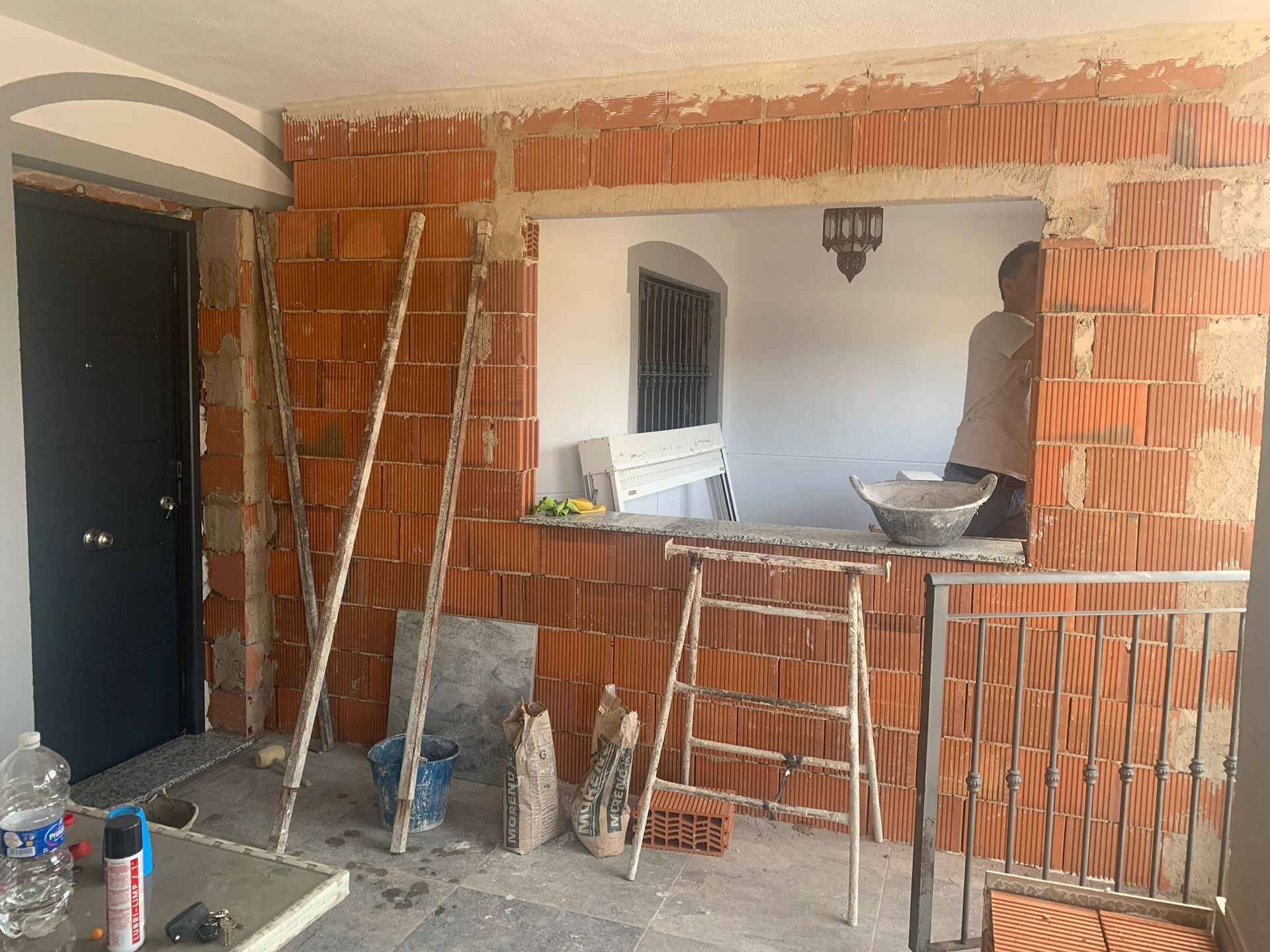 Construcción en progreso: Se están construyendo muros de ladrillo alrededor de una puerta y una ventana. Una persona trabaja cerca con herramientas.