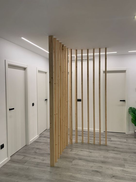 Biombo divisorio de listones de madera en pasillo blanco con puertas.