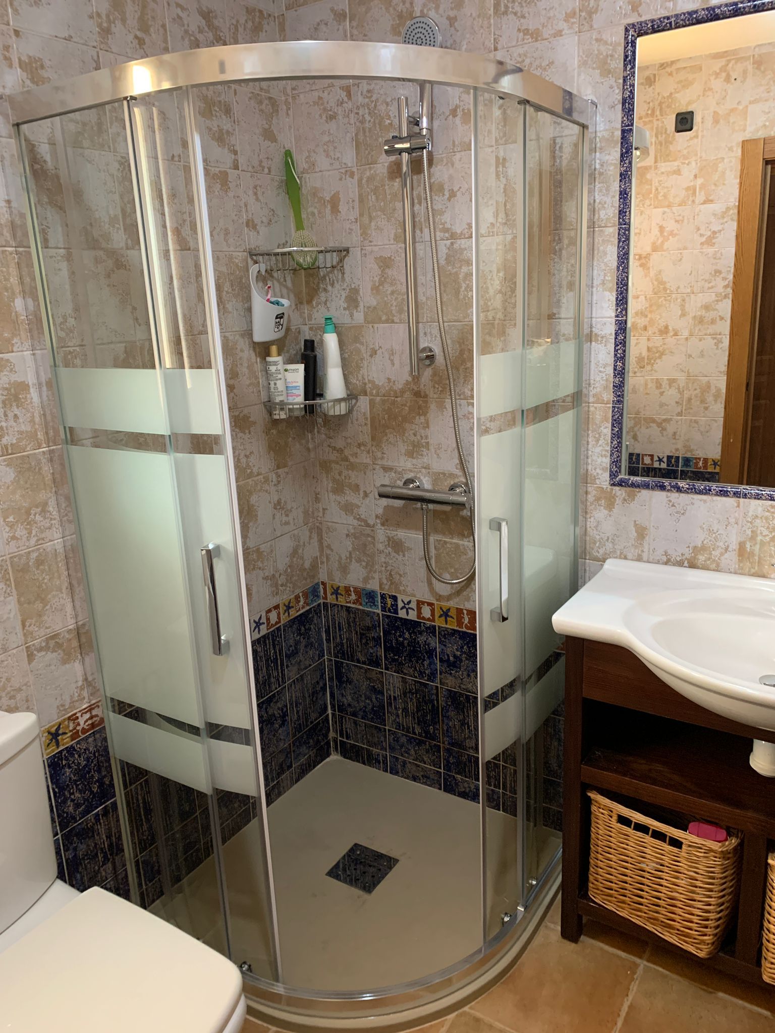 Ducha con puertas de cristal, paredes de azulejos beige y lavabo con mueble de madera oscura.