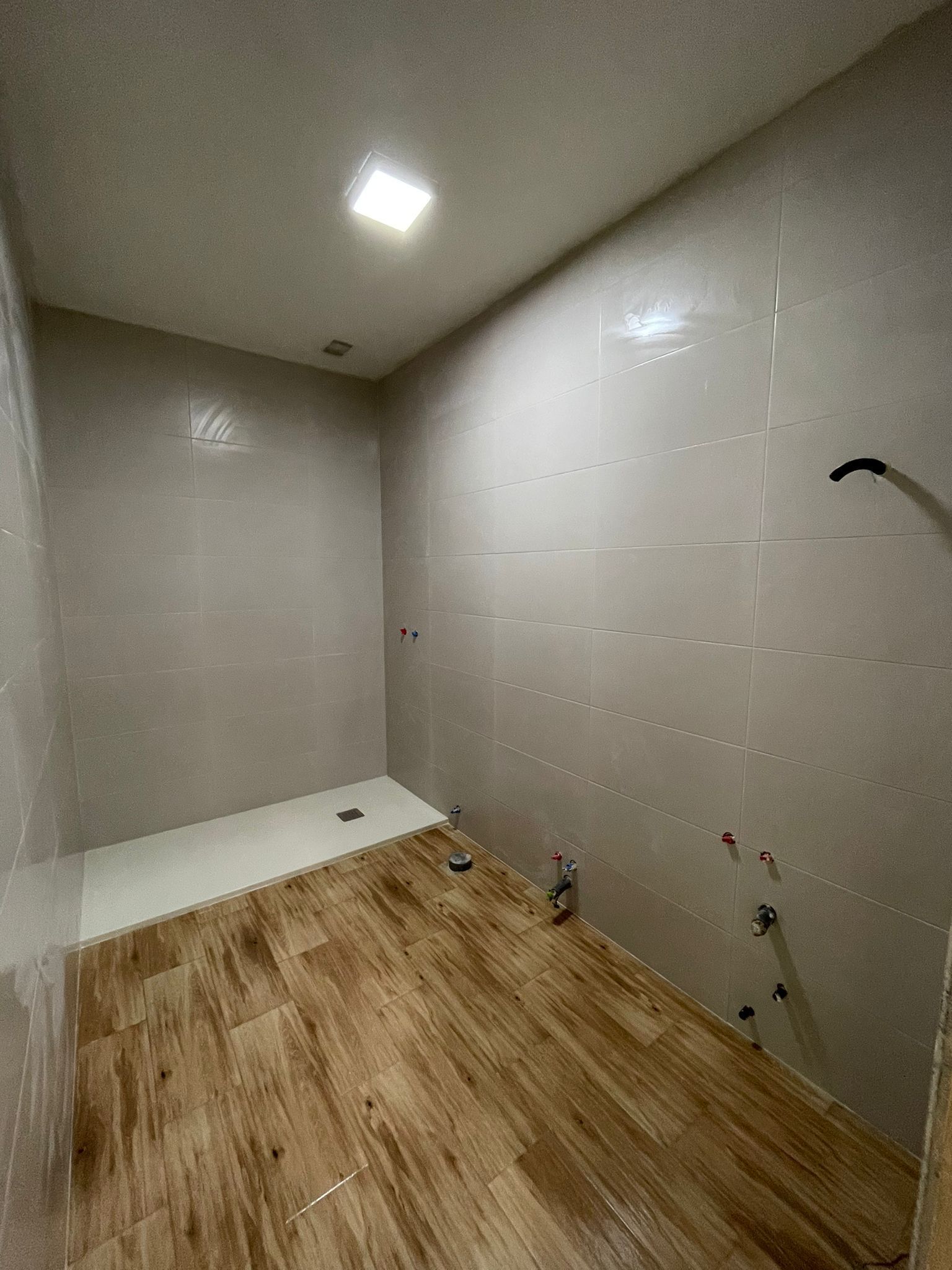 Baño con paredes alicatadas, suelo imitación madera, zona de ducha, grifería a la vista.