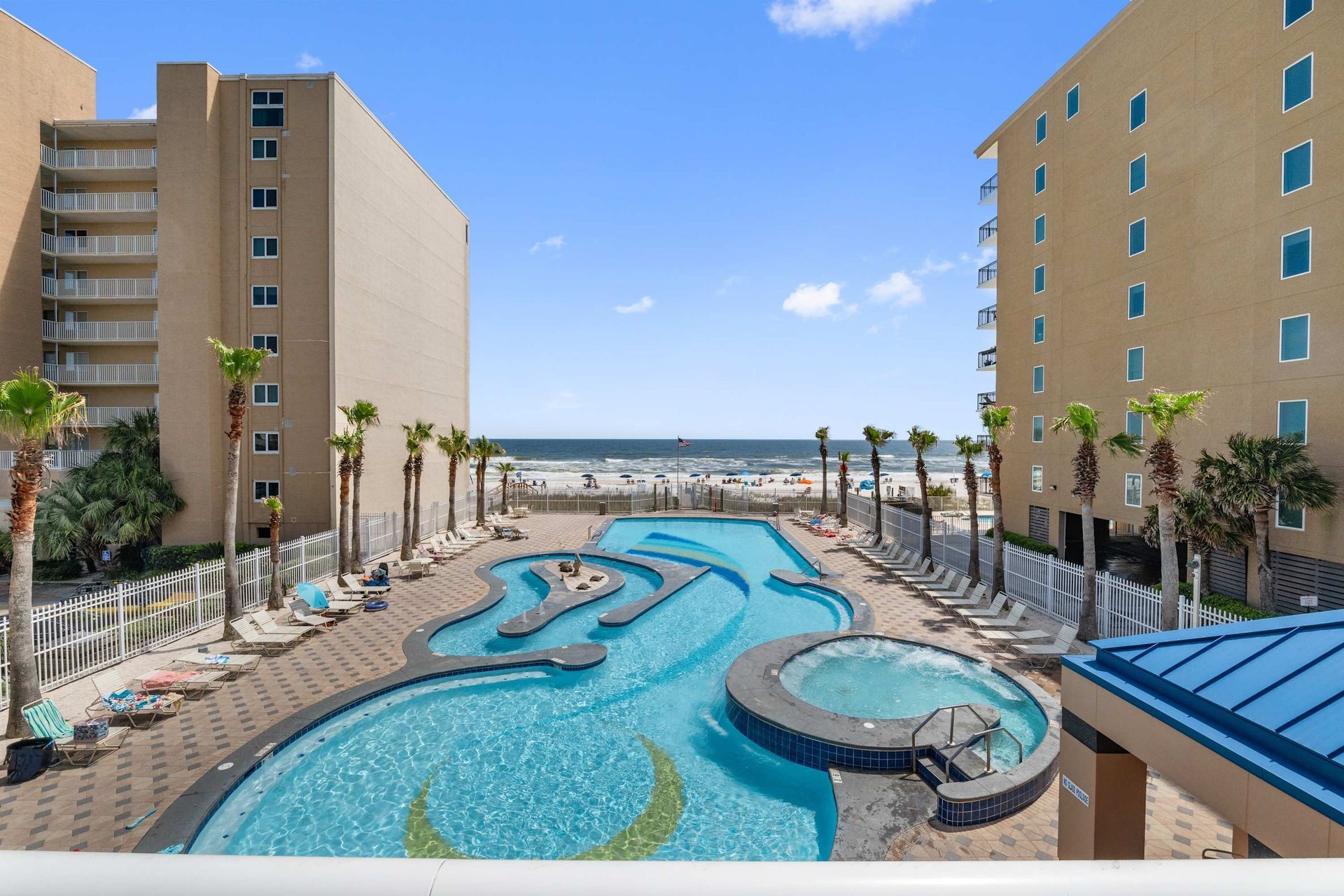 Beachside pool with a lazy river and hot tub. Turquoise water, palm trees, and lounge chairs.