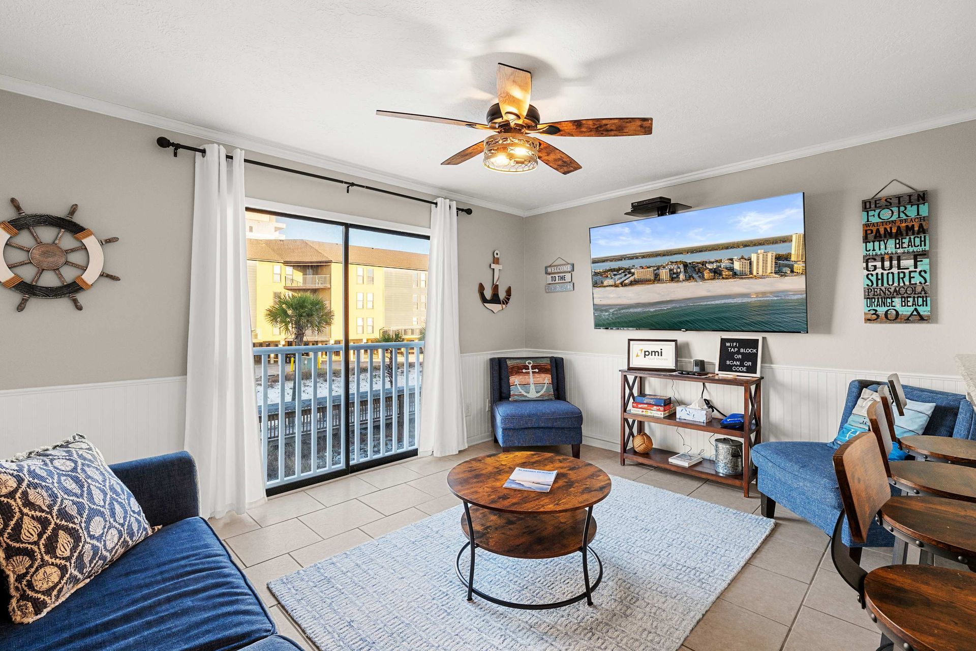 Living room with coastal decor: blue sofa, round coffee table, TV, and beach view.