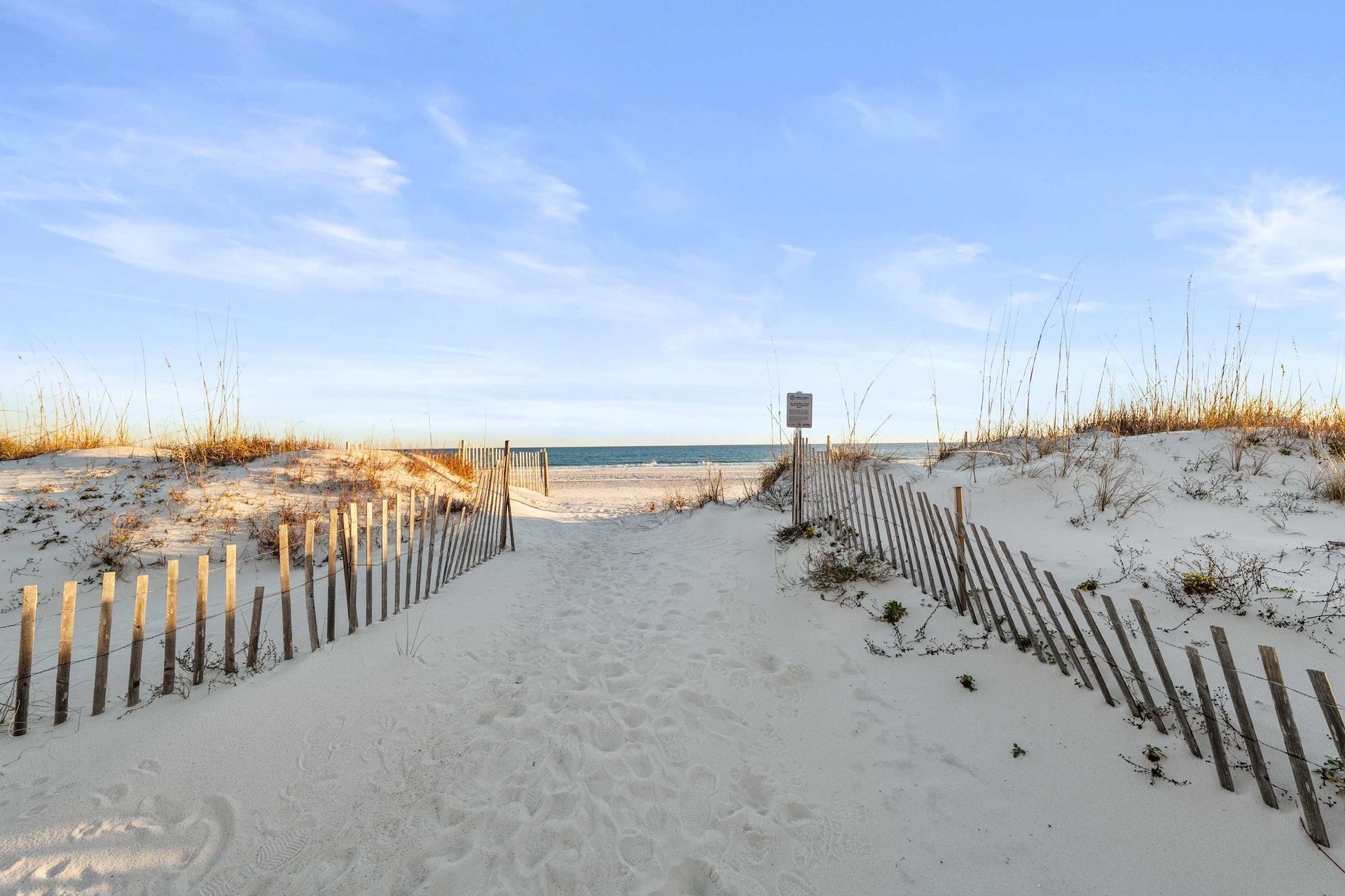 Sandy path through dunes leads to the gulf and white sand beaches with blue sky overhead.